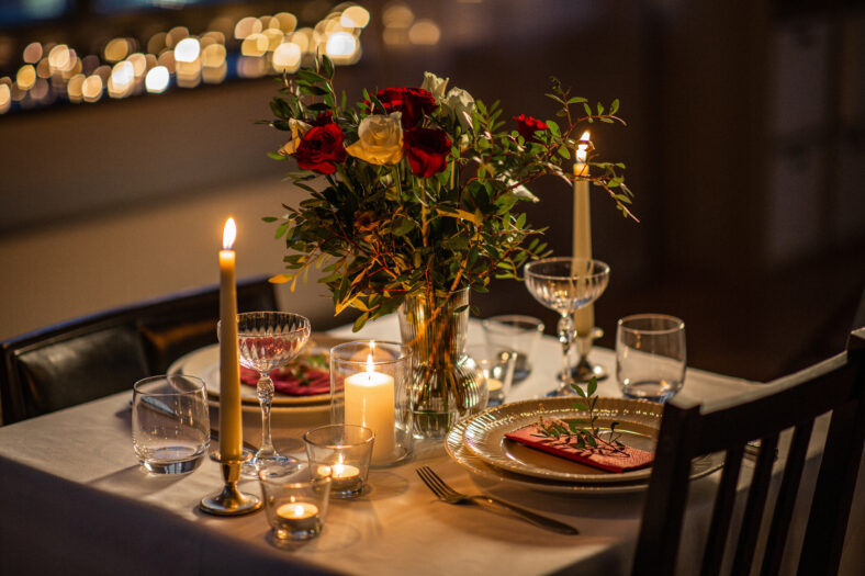 holidays, romantic date and celebration concept - close up of festive table serving for two with flowers in vase and candles burning at home on valentine's day