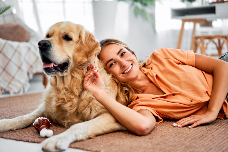 Love and affection. Beautiful young lady with blond hair resting on floor with lovely dog companion. Smiling caucasian woman enjoying home comfort while leaning back on fluffy golden retriever.