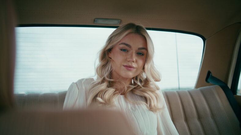 Gorgeous blonde sitting at automobile back seat looking camera close up. Portrait of beautiful happy lady traveler relaxing in retro car. Carefree cute girl passenger posing inside classic auto salon.