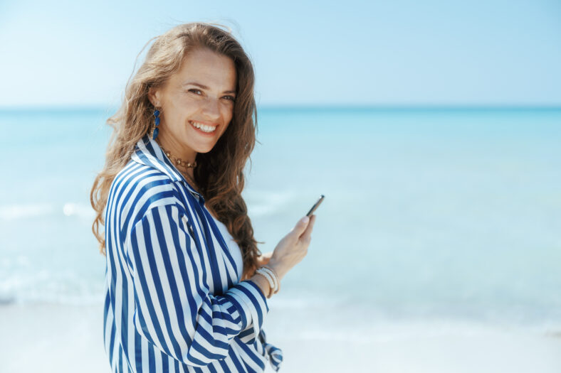 happy modern middle aged woman on the seashore with smartphone.