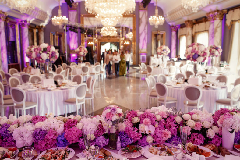 Look at the table for the table, which is decorated with garland made of pink and white flowers in a large evening hall