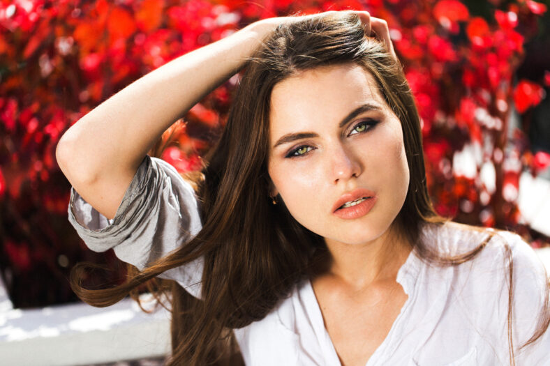 Stunning green-eyed woman sits before red flowers