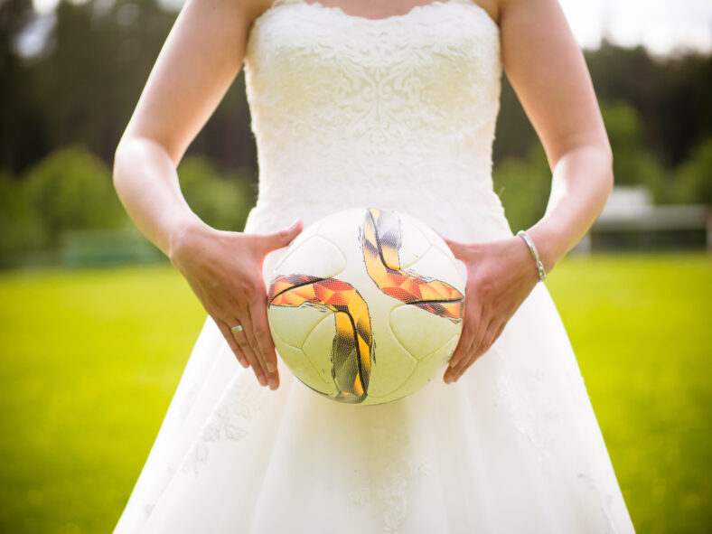 The bride holds the football in hands on the football field