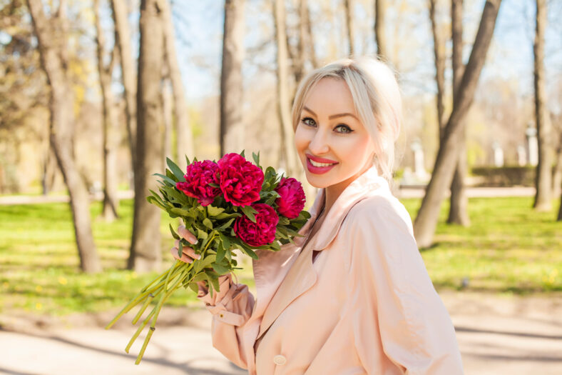 Mujer sonriente con flores al aire libre. Alegre modelo femenina con peonía en el parque