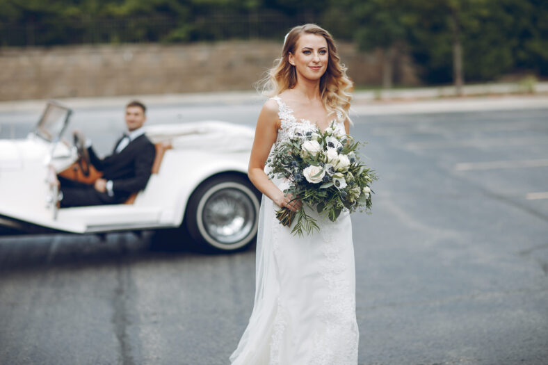 Beautiful bride in a long white dress. Handsome groom in a black suit. Couple near old car