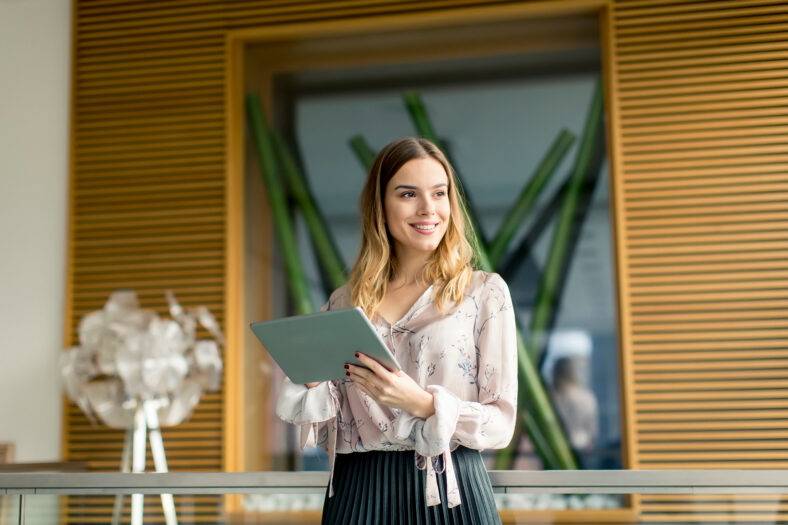 Atractiva joven empresaria que usa una tableta digital mientras está de pie en la oficina