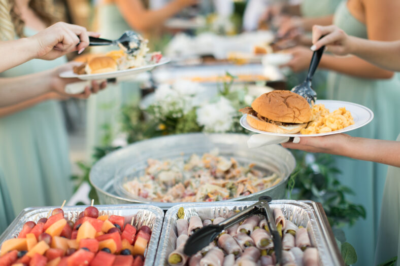 Close up of bridal party dishing up catered buffet food at casual outdoor wedding