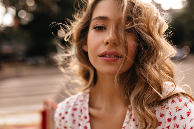 Close-up of mysterious caucasian young lady with imposing facial expression looking at camera. Gorgeous blonde looks at camera wearing white blouse. Happiness summer lifestyle concept.