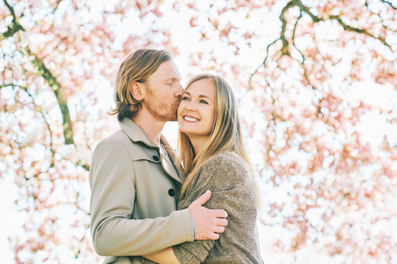 Feliz pareja romántica besándose bajo el árbol floreciente