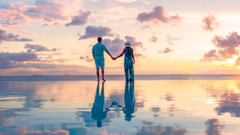 Hombres y mujeres jóvenes que miran la puesta de sol con reflejo en la piscina infinita en Saint Lucia Caribbean, una pareja en Infinity Pool durante el atardecer con una colorida puesta de sol en el océano