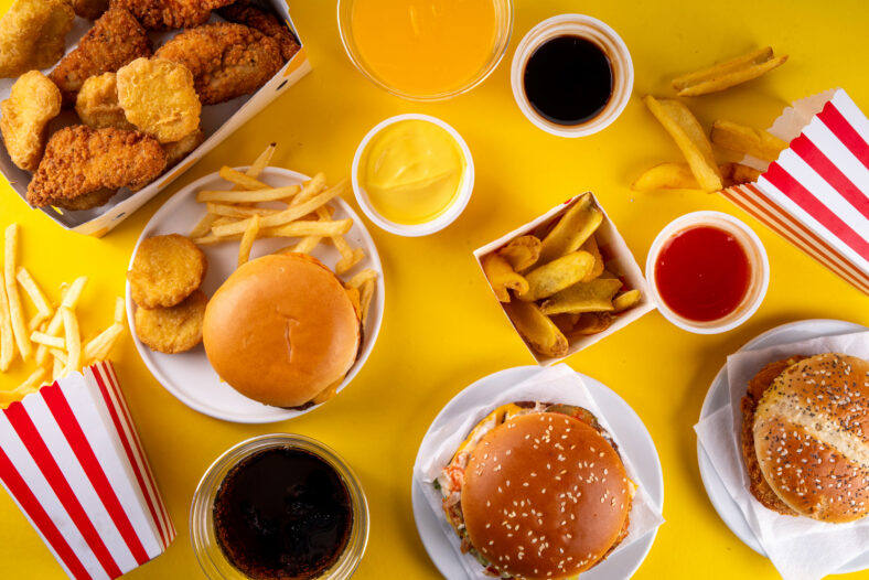 Latar belakang makanan cepat saji dengan berbagai burger, cheeseburger, nugget, kentang goreng, minuman soda bersoda. Sampah makanan cepat saji yang tidak sehat, makanan olahan ultra dengan nutrisi rendah, nilai kalori tinggi